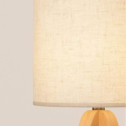 ooden tripod base table lamp with beige fabric drum shade, softly glowing in a cozy interior setting.