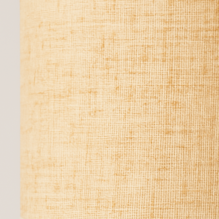 Cylindrical beige fabric table lamp with wood base and grey trim accents, glowing softly against a neutral studio background.